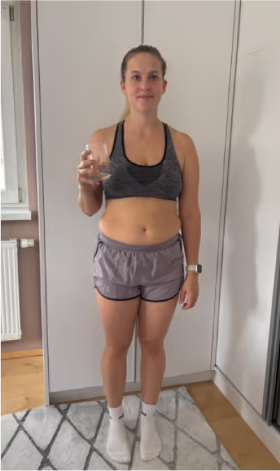 Eine Frau im Sport-BH und Shorts steht vor einem Schrank und hält ein Glas.