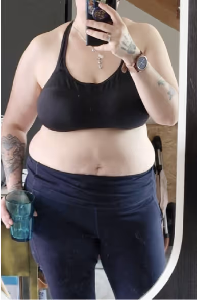 Eine Frau in Sport-BH und Leggings macht ein Selfie im Spiegel und hält ein Glas.