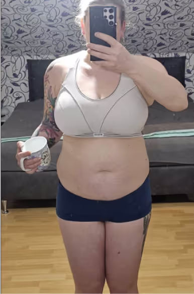 Eine Frau in Sport-BH und Shorts macht ein Selfie im Spiegel und hält eine Tasse.