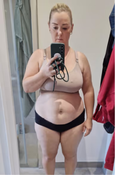 Eine Frau in Sport-BH und Unterwäsche macht ein Selfie im Spiegel.