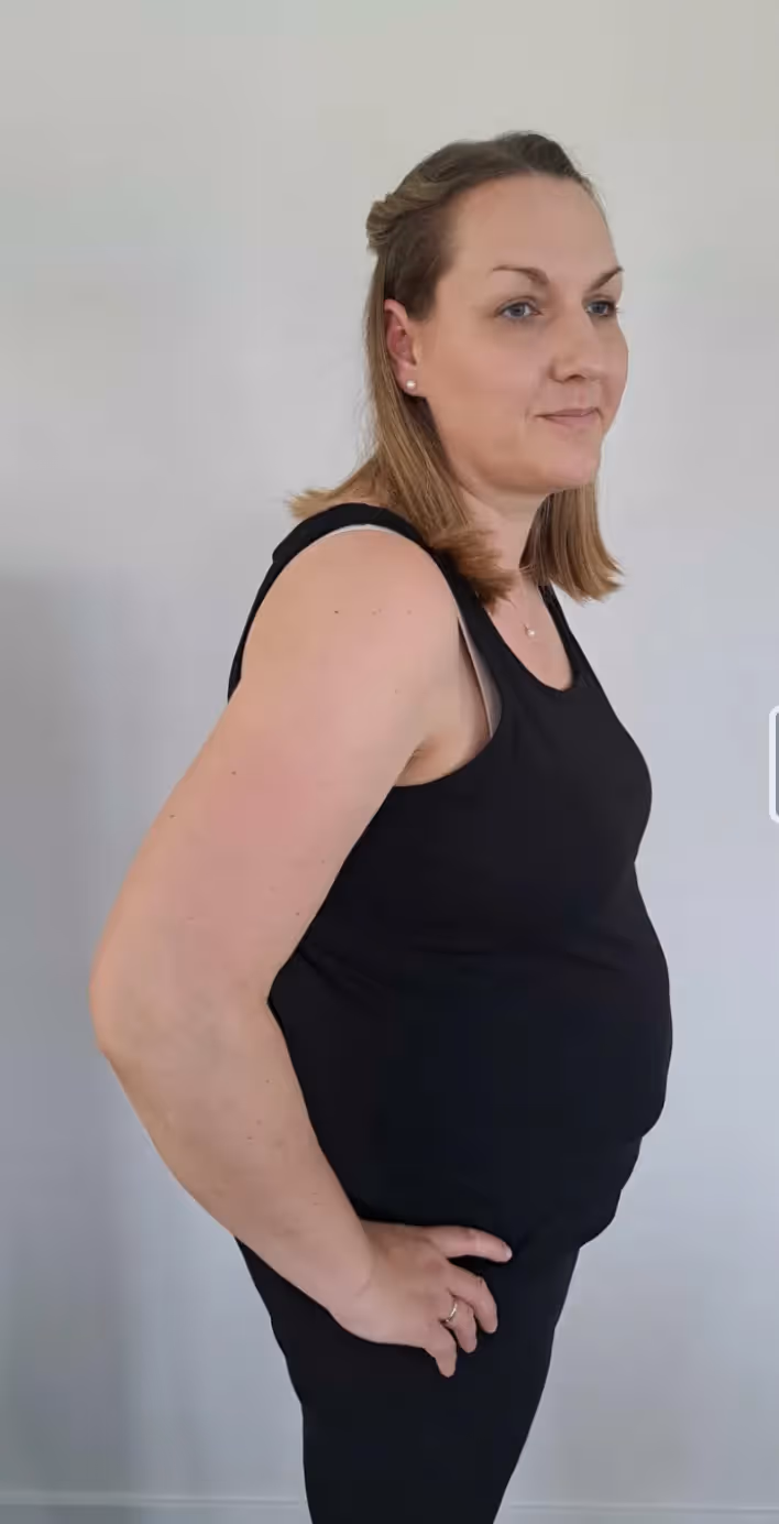 Eine Frau mit einem Dutt und seitlich hochgesteckten Haaren steht lächelnd vor einer weißen Wand.